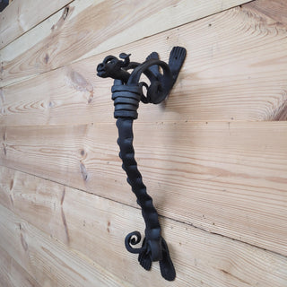 Side view of a rustic wrought iron door pull with a twisted shaft and bull head top, fixed to a wooden surface