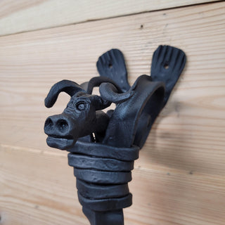 Close-up of a hand-forged wrought iron door handle featuring a detailed bull head design, mounted on wooden door panels.