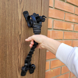 Forged iron bull head handle attached to a rustic barn door, showing the full shape and mounting brackets.