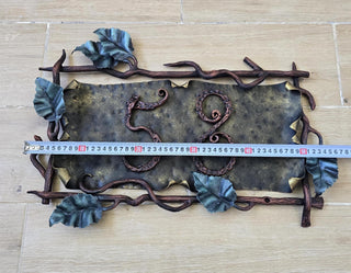 Hand-forged wrought iron house number sign with vines and leaves, displaying the number 58 on a wooden wall