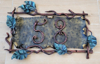 Hand-forged wrought iron house number sign with vines and leaves, displaying the number 58 on a wooden wall