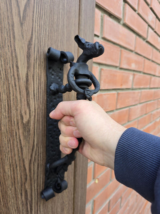 Hand holding the dog-shaped door pull attached to a wooden door.