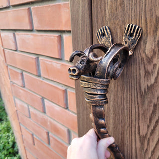 Hand holding forged bull head handle on rustic wooden door