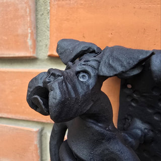 Forged iron door handle shaped like a boxer dog mounted on a brick wall.