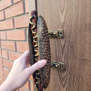 Unique iron door pull in the shape of a hot dog, mounted on a wooden door