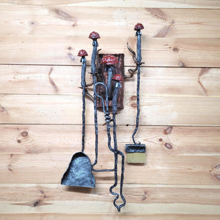 Hand-forged iron fireplace tools with red mushroom handles on wooden wall