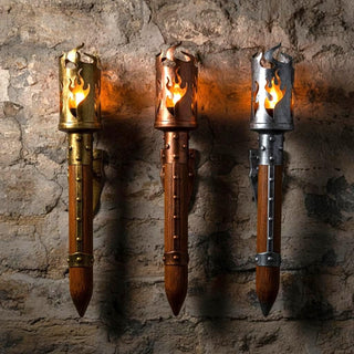 Three medieval wall torch sconces in antique gold, aged copper, and dark silver finishes, handcrafted iron and wood flame lanterns mounted on a stone wall